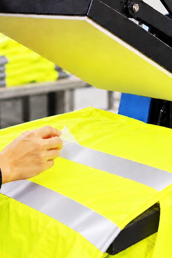 Reflexband zum Aufbügeln wird mit der Transferpresse auf Sicherheitskleidung aufgebracht